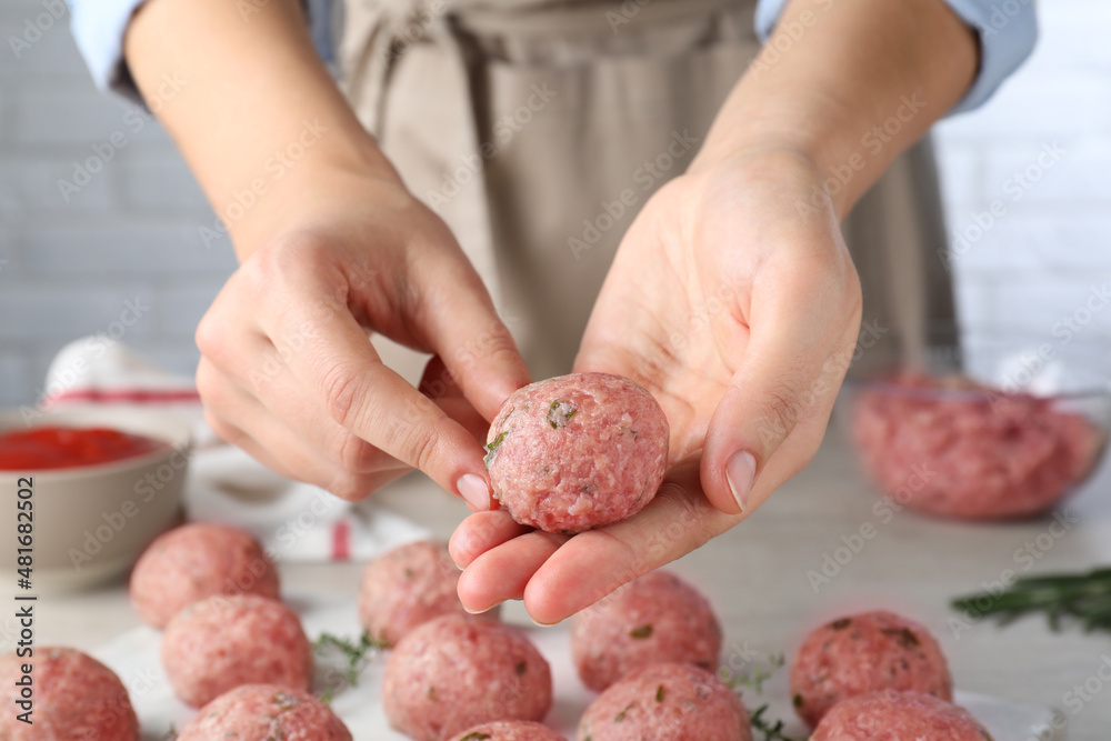 Woman making fresh raw meatballs at white table indoors, closeup