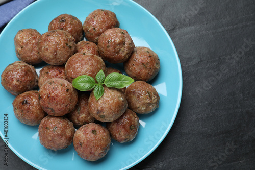 Tasty cooked meatballs with basil on black table, top view
