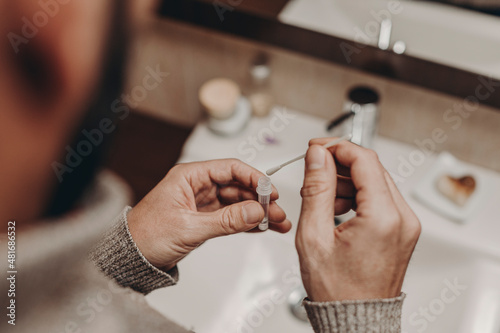man inserting nasal swab into liquid of covid test in bathroom