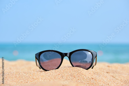 Closeup of black protective sunglasses on sandy beach at tropical seaside on warm sunny day. Summer vacation concept