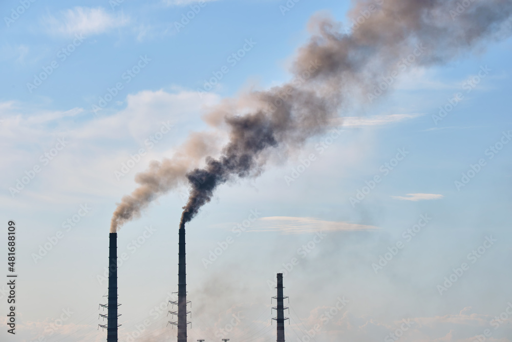 Closeup of thermal power plant high pipes with black smoke moving upwards polluting atmosphere. Production of electrical energy with fossil fuel concept Closeup of thermal power plant high pipes with black smoke moving upwards polluting atmosphere. Production of electrical energy with fossil fuel concept
