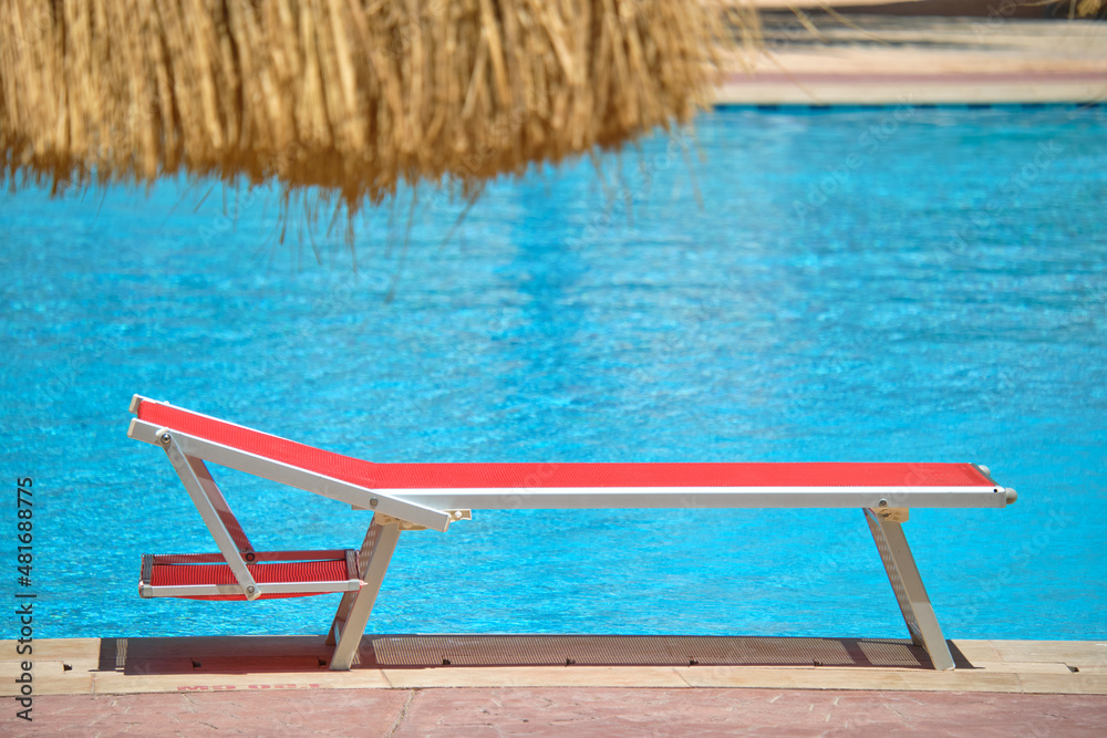 Fototapeta premium Empty deck chair on swimming pool side in summer resort. Vacations and getaway concept
