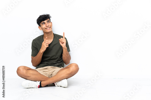 Young Argentinian man sitting on the floor pointing with the index finger a great idea