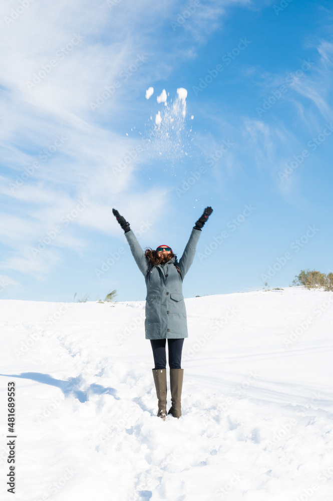 Beautiful woman throwing snowballs into the sky on a sunny vacation day in the snow
