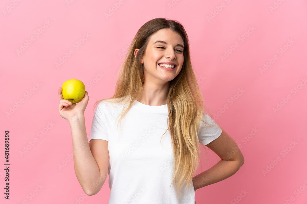 Young blonde woman isolated on pink background with an apple and happy Young blonde woman isolated on pink background with an apple and happy