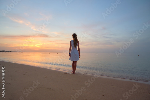 Lonely young woman standing on sandy beach by seaside enjoying warm tropical evening © bilanol