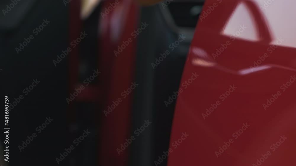 The woman brings her hand to the red handle of the car door, opens it and sits in it in a brown coat. The woman brings her hand to the red handle of the car door, opens it and sits in it in a brown coat.