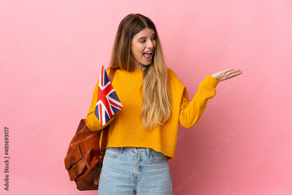 Young blonde woman holding an United Kingdom flag isolated on white background extending hands to the side for inviting to come Young blonde woman holding an United Kingdom flag isolated on white background extending hands to the side for inviting to come