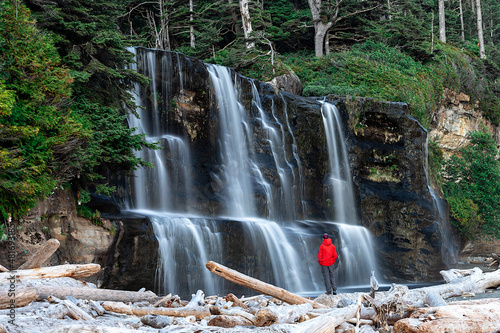 Hiker figure wearing a red jacket in front of Tsusiat Falls along the West Coast Trail, Pacific Rim National Park, British Columbia, Canada.