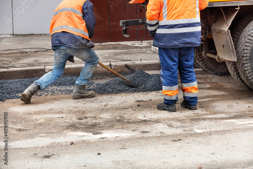 A road maintenance worker distributes fresh asphalt with a shovel at the patching of the road.
