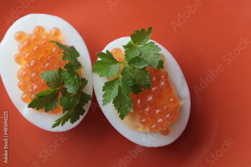 Red caviar with parsley lies on boiled and chopped eggs on a plate, top view.	