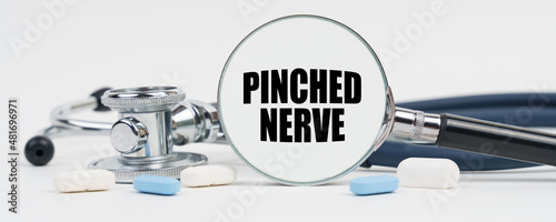 On a white surface are pills, a stethoscope and a magnifying glass inside which is written - Pinched nerve photo