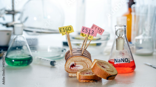 Food additives: sweet roll with chemical additives with colored labels, on a laboratory table. Close up. photo