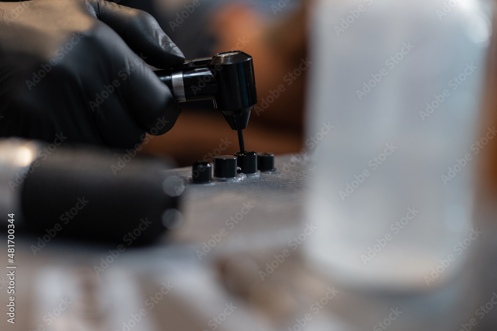 Professional man tattoo artist in black gloves with a mixer mixes paint and ink in tubes, close-up. Preparation for creating a tattoo