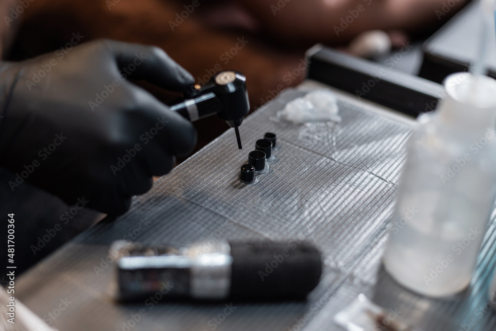 Professional male tattoo artist in black gloves makes ink and mixes paints using a mixer in the studio. Workspace of a tattoo artist. Tattoo preparation process