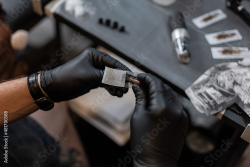 Professional male tattoo artist with black gloves take out the needle from the package and prepares to get a tattoo. Workspace in tattoo studio