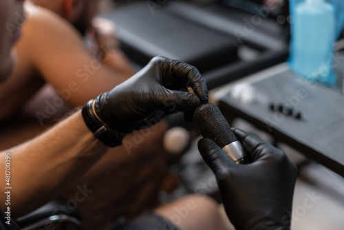 Professional tattoo artist in black gloves puts a needle on a modern tattoo machine, close-up. Preparation process before tattooing. Start tattoo