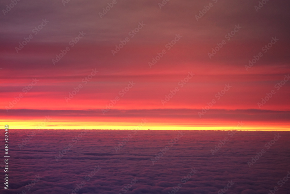 Sunset on cloudy sky as seen from a window plane above fluffy clouds