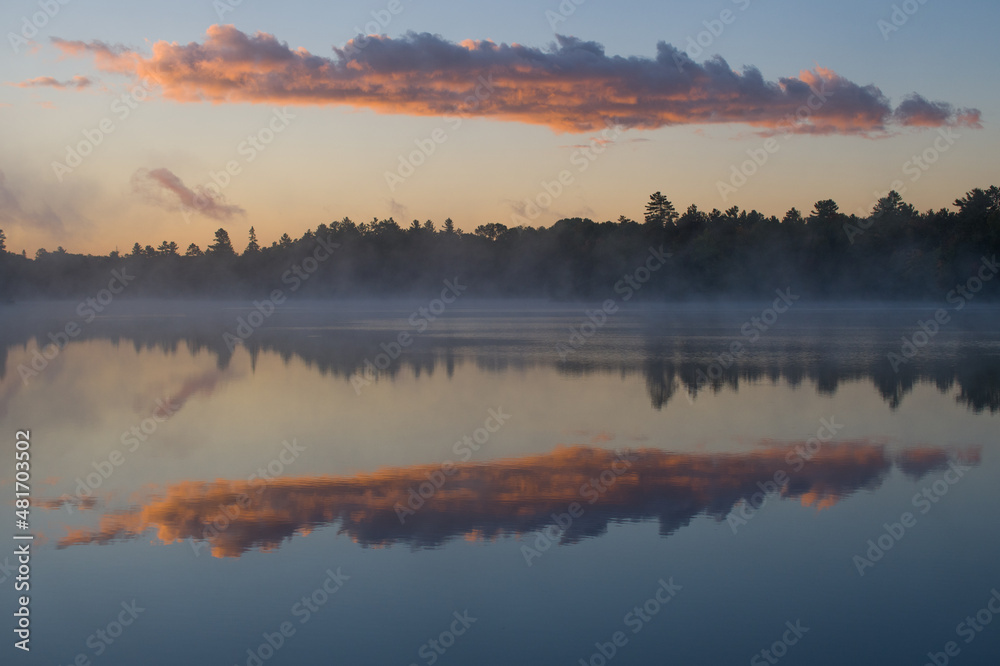 Fototapeta premium clouds reflecting on calm water morning mist hovering over lake at sunrise early morning fog or mist trees forest or woods reflecting in tranquil calming lake water blue sky purple clouds horizontal