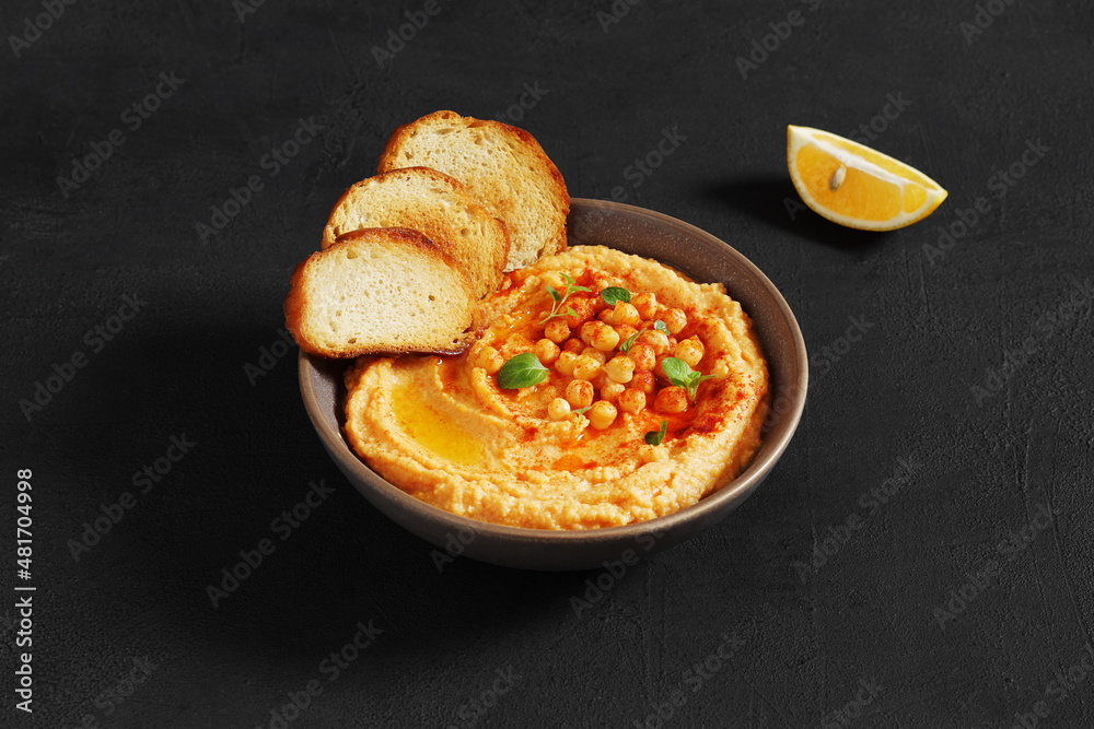 An appetizer Hummus served with fresh pita bread and herbs, seasoned with extra virgin olive oil and paprika in vintage ceramic plate on the dark background An appetizer Hummus served with fresh pita bread and herbs, seasoned with extra virgin olive oil and paprika in vintage ceramic plate on the dark background
