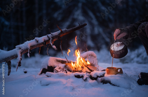 Pouring freshly brewed coffe from a kettle, brewed over a campfire in a snow-covered forest