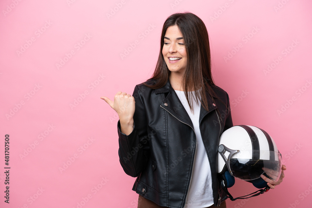 Young Brazilian woman with a motorcycle helmet isolated on pink background pointing to the side to present a product Young Brazilian woman with a motorcycle helmet isolated on pink background pointing to the side to present a product