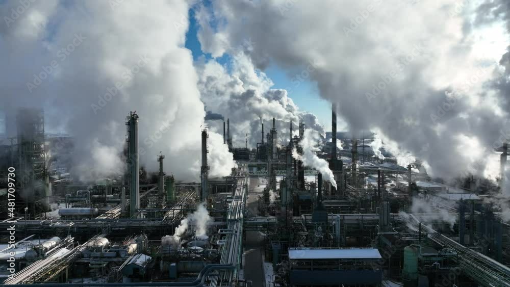 Smoke billowing from oil refinery plant on winter day. Stock drone footage with camera zooming out above petrochemical processing complex.