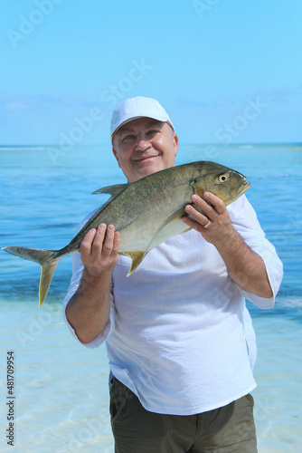 A large man holds a freshly caught fish on the shore of the Indian Ocean.
