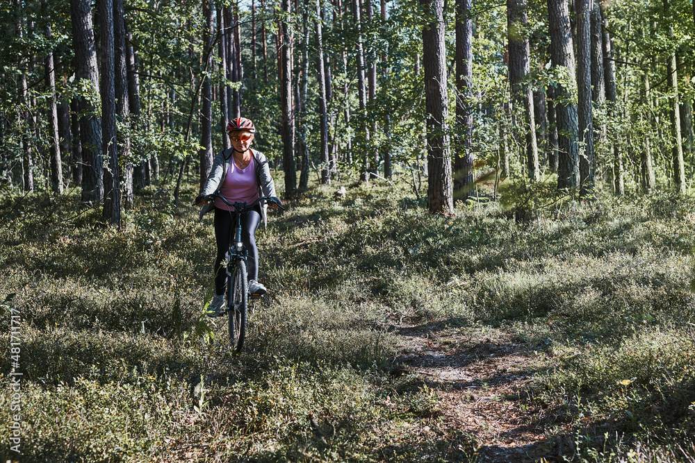 Active woman cycling on forest road. Female riding bicycle off-road route on summer vacation day. Woman wearing bicycle helmet and gloves