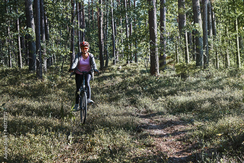 Active woman cycling on forest road. Female riding bicycle off-road route on summer vacation day. Woman wearing bicycle helmet and gloves