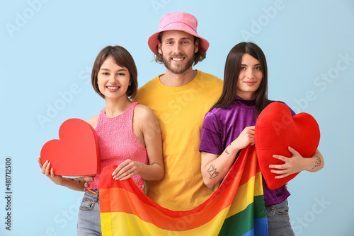 Man and two beautiful women with rainbow flag and red hearts on color background. Concept of polyamory and LGBT