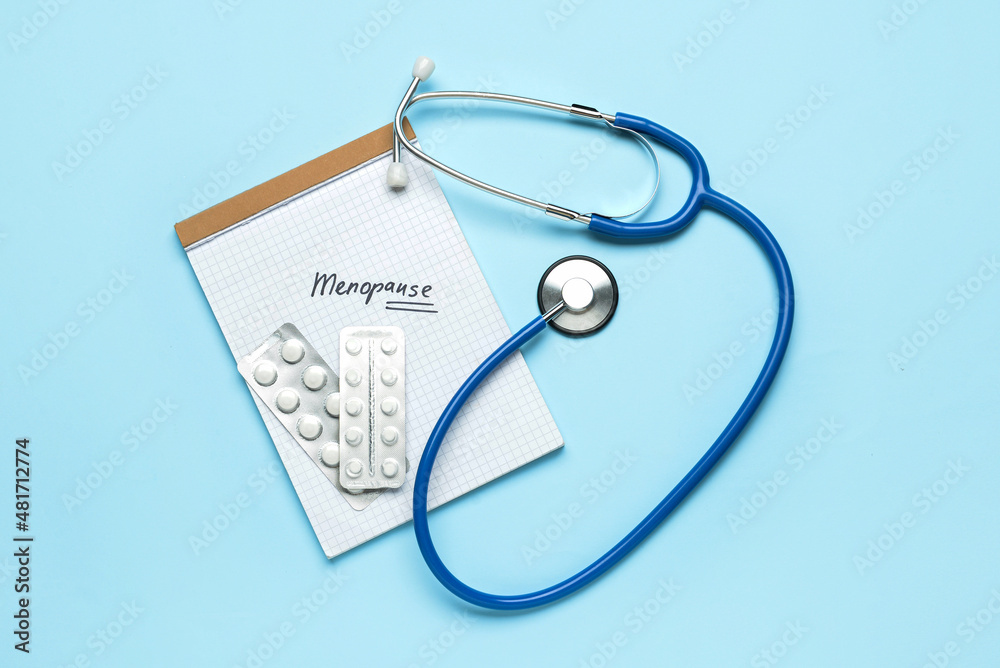 Notebook with word MENOPAUSE, pills and stethoscope on blue background Notebook with word MENOPAUSE, pills and stethoscope on blue background