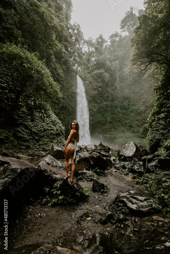 A young woman traveller is exploring a waterfall in tropical settings of Bali islands, Indonesia. Tropical forest, lush greenery, rive