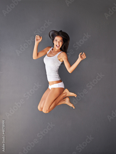 You've got to make life exciting. Full-length shot of a happy young woman jumping against a gray background. photo
