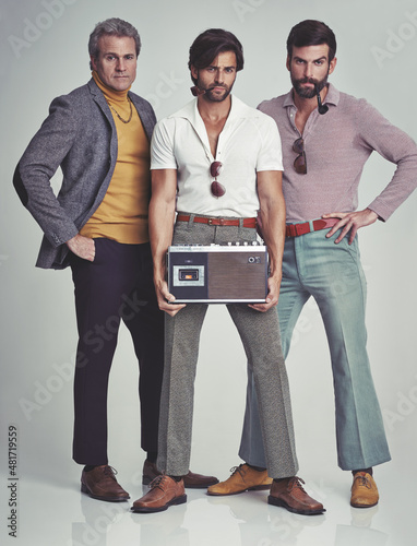 Ready to kick it retro style. A studio shot of three men clad in retro 70s wear holding a cassette player.