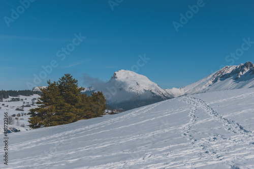 A picturesque landscape view of the snowcapped French Alps mountains with a hiking path in the snow on a cold winter day (La Joue du Loup, Devoluy)