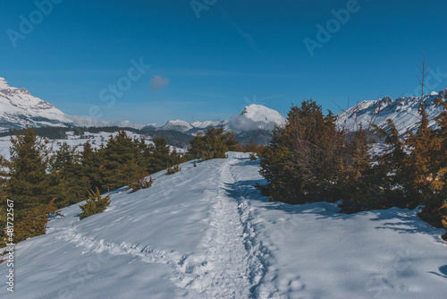 A picturesque landscape view of the snowcapped French Alps mountains with a hiking path in the snow on a cold winter day (La Joue du Loup, Devoluy) © k.dei
