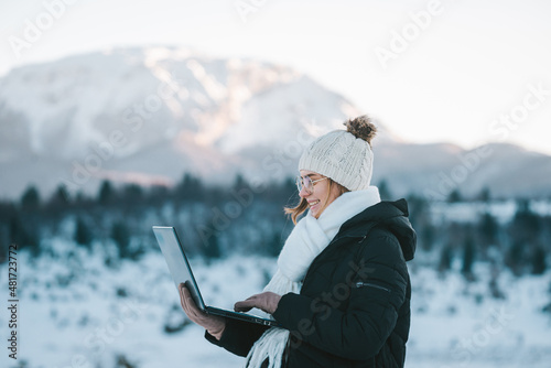 young smiling woman freelancer using laptop outdoors in snow mountains