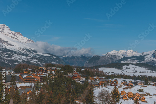 A picturesque landscape view of the snowcapped French Alps mountains and the ski resort buildings on a cold winter day (La Joue du Loup, Devoluy)