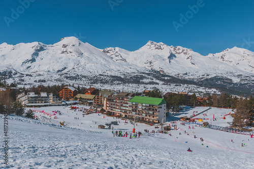 A picturesque landscape view of the snowcapped French Alps mountains and the ski resort buildings on a cold winter day (La Joue du Loup, Devoluy)