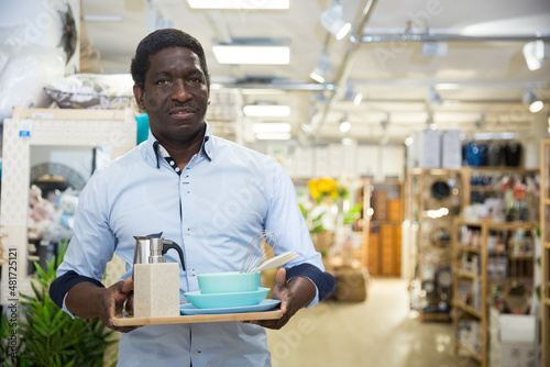 Satisfied african american male shopper holding dishware and kitchen accessories bought in household goods shop