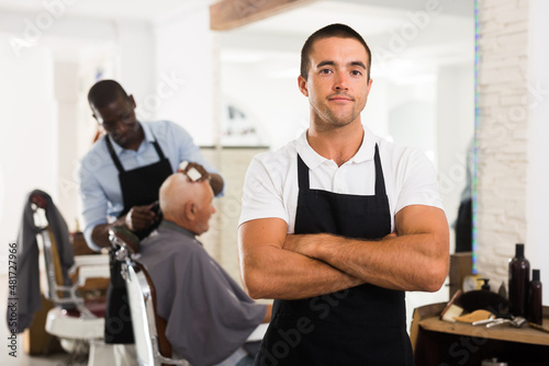 Portrait of successful professional young barber standing in hair salon..