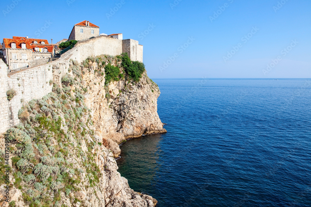 Fortified wall of Dubrovnik on the rock, orange roofs, and Adriatic sea in Croatia