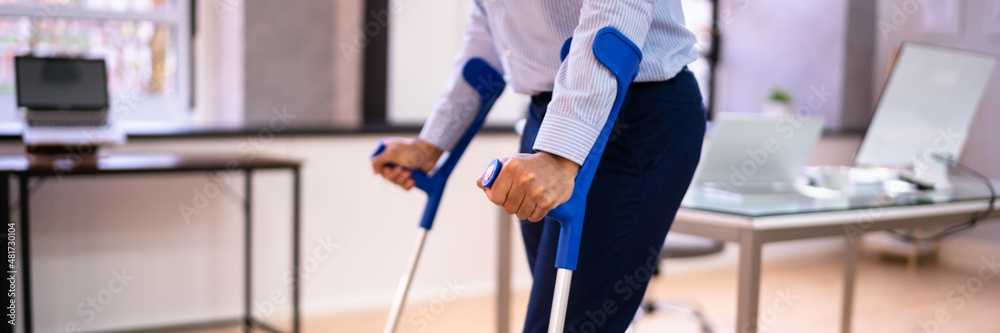 Worker With Crutches At Workplace Or Office Worker With Crutches At Workplace Or Office