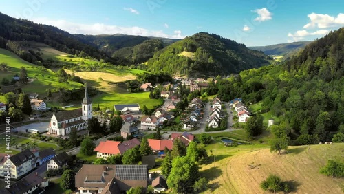 Idyllic little town with a church in a scenic valley in Germany, surrounded by hills, meadows and forests, aerial footage with blue sky and sunshine
 photo