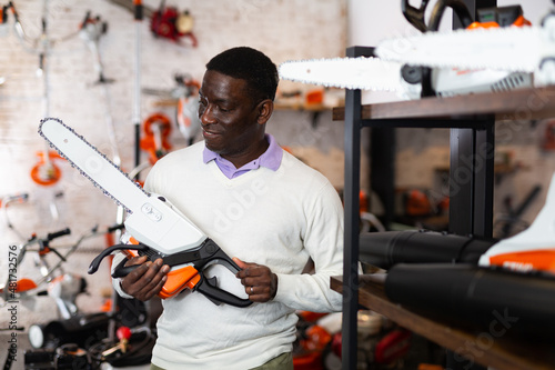 African american man chooses chainsaw at a garden tool store