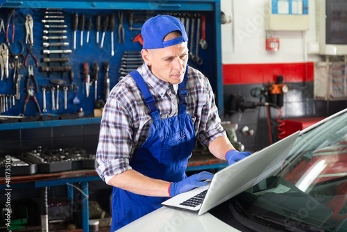 Auto mechanic in blue uniform doing engine diagnostics with computer in the car service