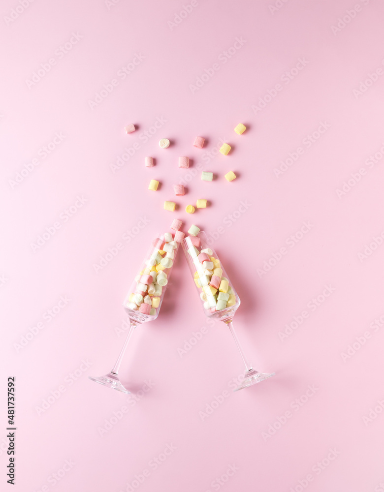 Two tall glass glasses with multicolored marshmallows clinking on a pink background. The concept of Valentine's Day.