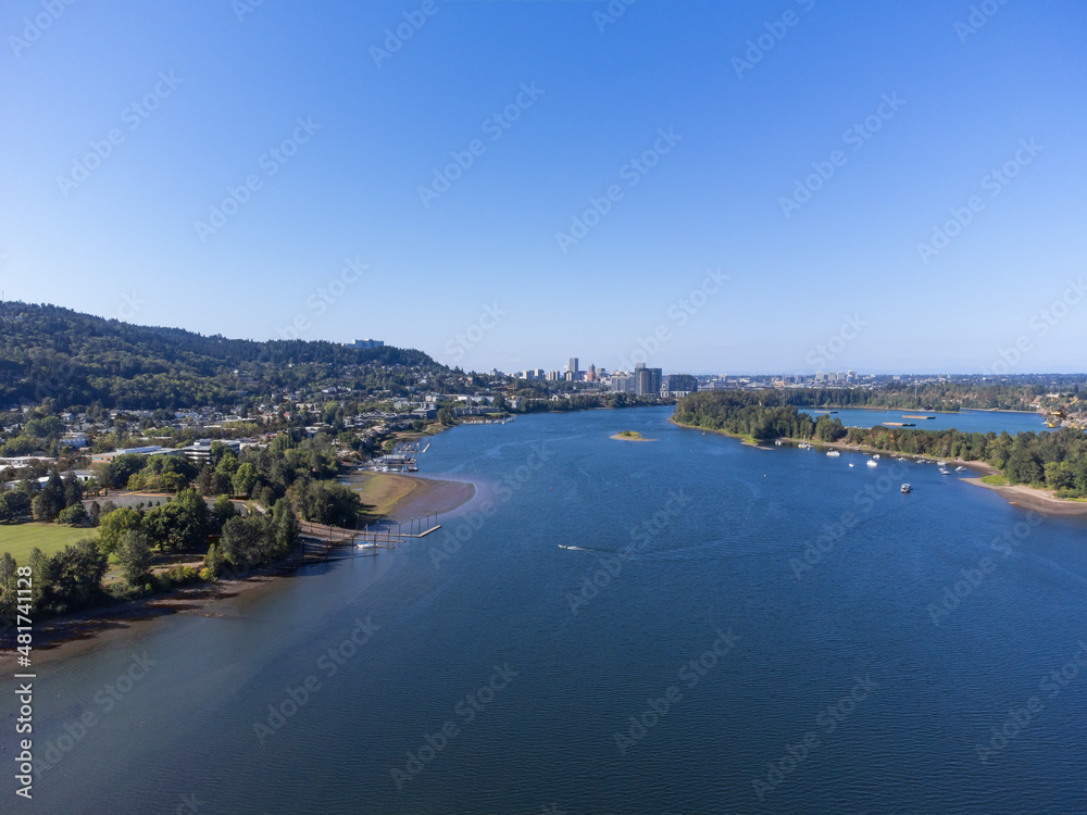 View from above. A small green city on the bank of a big blue river. Mountains, clear cloudless sky. There are many boats on the river. Ecological place, map, planning, housing issue.