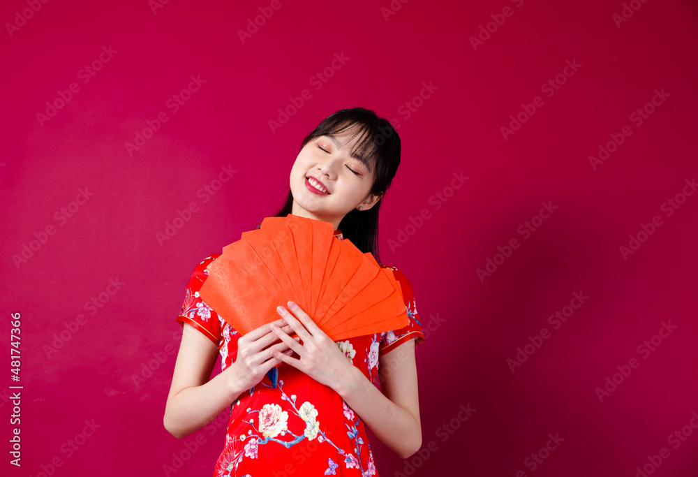 Beautiful Asian girl in traditional cheongsam on red background holding red envelope. Beautiful Asian girl in traditional cheongsam on red background holding red envelope.